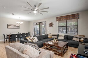 A living room with a sofa, a coffee table, a dining area with chairs, a chandelier, and a ceiling fan. - Family retreat w/ pool, hot tub, & resort access (Four Corners)