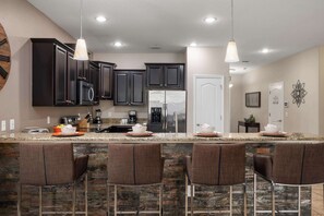 A kitchen with dark cabinets, a granite countertop, and a bar area with four stools. - Family retreat w/ pool, hot tub, & resort access (Four Corners)