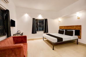 A hotel room with a bed, a red sofa, a small table, and a window with curtains. - Deluxe With Ganga View Hotel Neatflix and Chill (Bhubaneshwar)