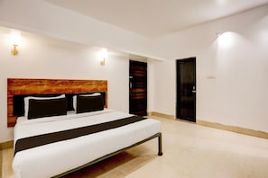 A modern hotel room with a large bed, a wooden headboard, and a door. - Deluxe With Ganga View Hotel Neatflix and Chill (Bhubaneshwar)