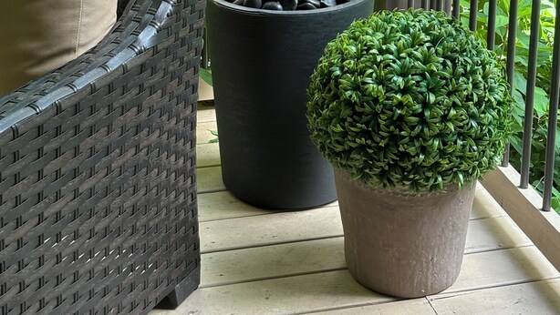 Un balcón con una silla de mimbre, dos plantas en macetas y una barandilla de madera.