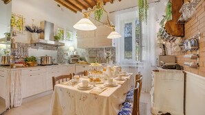 A kitchen with a dining table set for a meal, wooden cabinets, and hanging plants. - Paradise Family Apartment | Hot Tub&Garden, Lucca, Italy (Lucca)