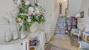 A room with a white ornate mirror, a floral arrangement, a staircase with blue and white tiles, and a chair with a cushion. - Paradise Family Apartment | Hot Tub&Garden, Lucca, Italy (Lucca)