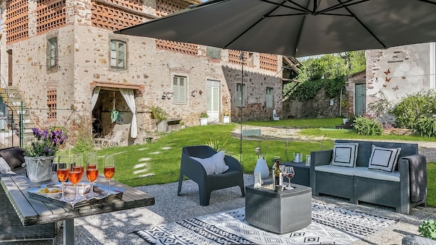 En udendørs terrasse med et bord til fire personer, en sofa og en parasol.