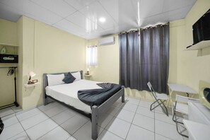 A hotel room with a bed, bedside tables, a desk, a chair, an air conditioning unit, and curtains. - Cheap Hotel Room in Sosua Center! (Sosúa)