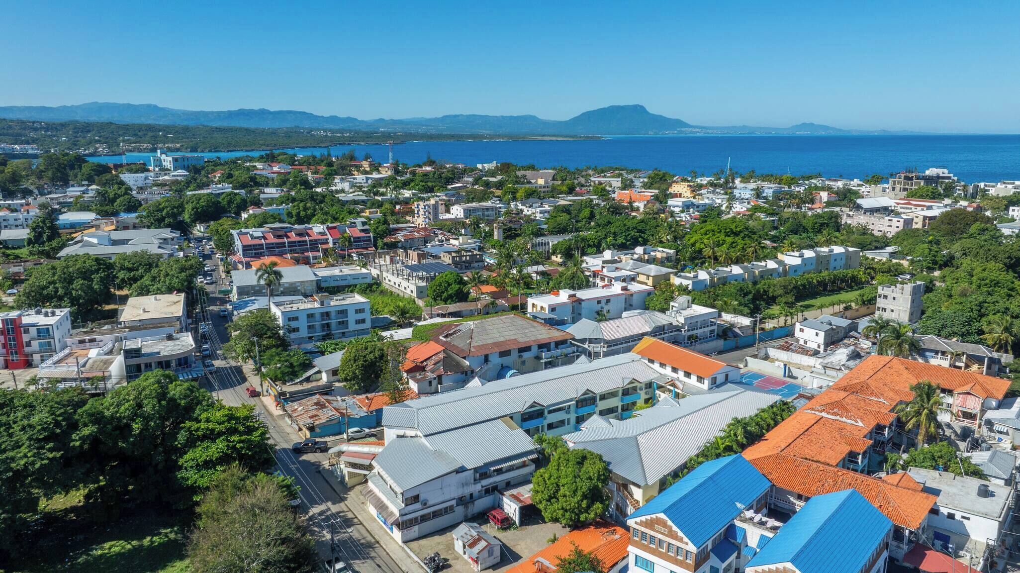 A coastal town with a mix of residential and commercial buildings, a clear view of the sea, and a hilly landscape in the distance.