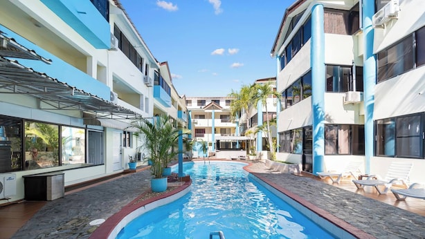 A swimming pool with a pool ladder, surrounded by lounge chairs and potted plants, with buildings on either side. - Cheap Hotel Room in Sosua Center! (Sosúa)