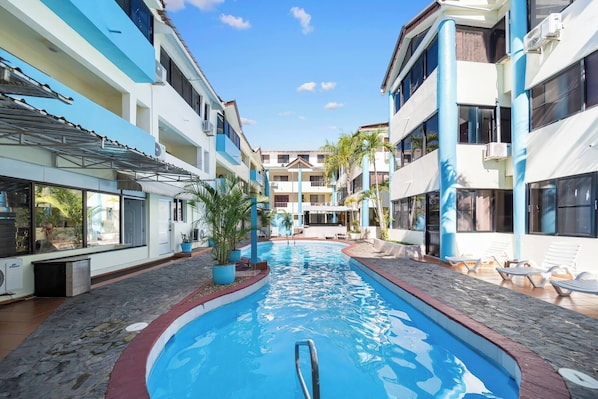 A swimming pool with a pool ladder, surrounded by lounge chairs and potted plants, with buildings on either side. - Cheap Hotel Room in Sosua Center! (Sosúa)