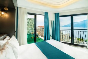 A hotel room with a bed, a balcony with a view of the sea, and a stone wall. - Gumus Yazar Hotel (Kaş)