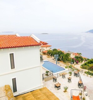 Un edificio con techo de tejas rojas, piscina, mobiliario exterior y vista al mar.
