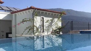 A swimming pool with clear water, a small building with a red roof, and a mountain in the background. - Gumus Yazar Hotel (Kaş)