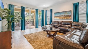 A living room with a leather sofa, a coffee table, and a view through glass doors to an outdoor patio. - Outdoor TV, Air Hockey, Foosball, Epic Game Room, Basketball Arcade, 1GB: Summer Breeze (Kissimmee)