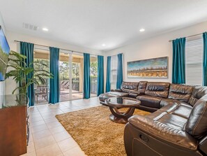 A living room with a leather sofa, a coffee table, and a view through glass doors to an outdoor patio. - Outdoor TV, Air Hockey, Foosball, Epic Game Room, Basketball Arcade, 1GB: Summer Breeze (Kissimmee)