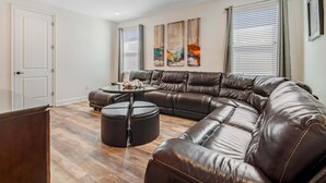 A modern living room with a sectional sofa, a round coffee table, and a large window with blinds. - Outdoor TV, Air Hockey, Foosball, Epic Game Room, Basketball Arcade, 1GB: Summer Breeze (Kissimmee)