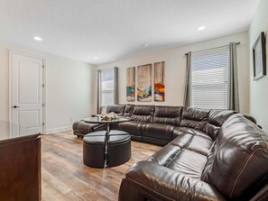 A modern living room with a sectional sofa, a round coffee table, and a large window with blinds. - Outdoor TV, Air Hockey, Foosball, Epic Game Room, Basketball Arcade, 1GB: Summer Breeze (Kissimmee)
