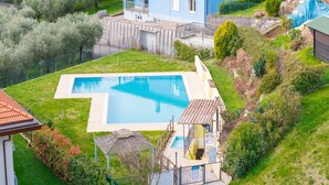 En bostadsträdgård med en swimmingpool, en liten täckt uteplats och ett hus med en balkong.