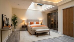 A bedroom with a skylight, a bed with pillows, a bedside table with a lamp, a plant, and a wardrobe. - Opulenti Mayfair 1BR Residence (London)