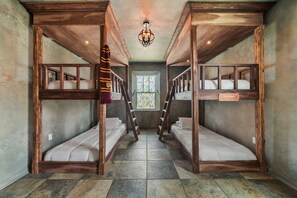 Ein Zimmer mit Etagenbetten, einer Holzbalkendecke, einem Chandelier und einem Glasfenster mit Bleiverglasung.