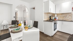 Eine moderne Küche mit weißen Schränken, ein Essbereich mit Tisch für zwei Personen und ein sichtbares Backrohr.