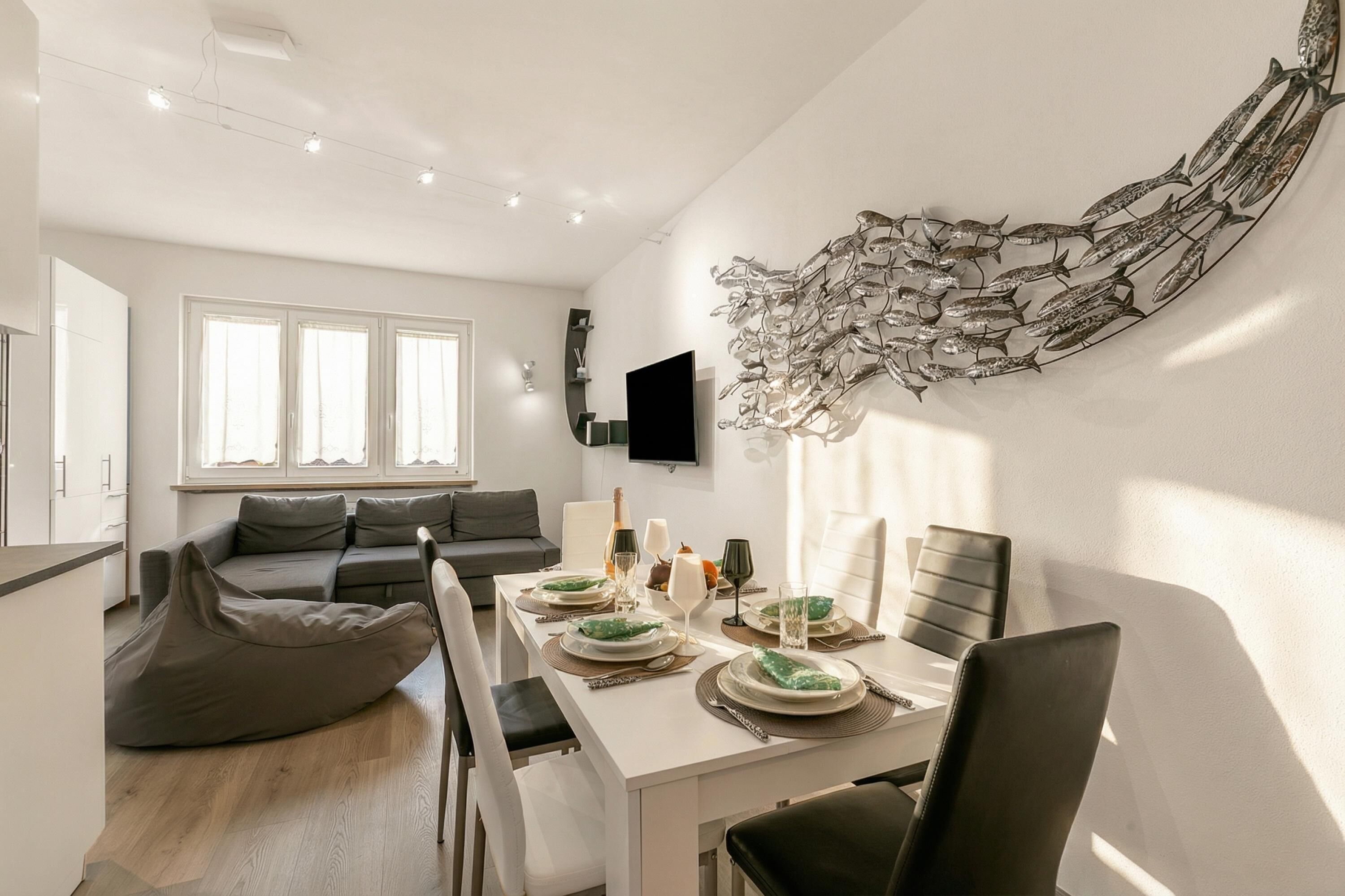 A modern living room with a dining area, a flat-screen TV mounted on the wall, and a large abstract wall art piece.