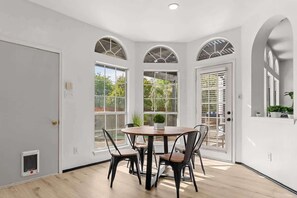A dining area with a round table and chairs, large windows, and a door. - Modern Oasis with Large Pool + Ping-Pong Sleeps 14 (McKinney)