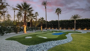 Um campo de golfe bem cuidado, com putting green, armadilhas de areia e lago.