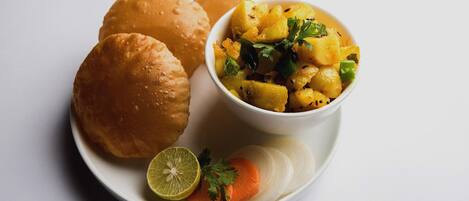 A plate with two bread rolls, a bowl of food, a lime, and sliced carrots.