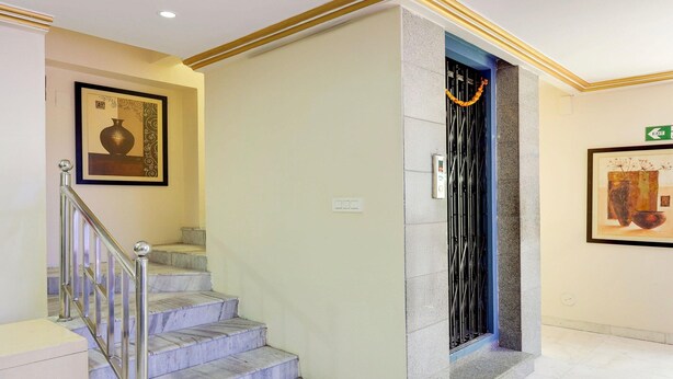 Una scalinata in marmo con ringhiera in metallo, un quadro incorniciato al muro e una porta con cancello decorativo in metallo.