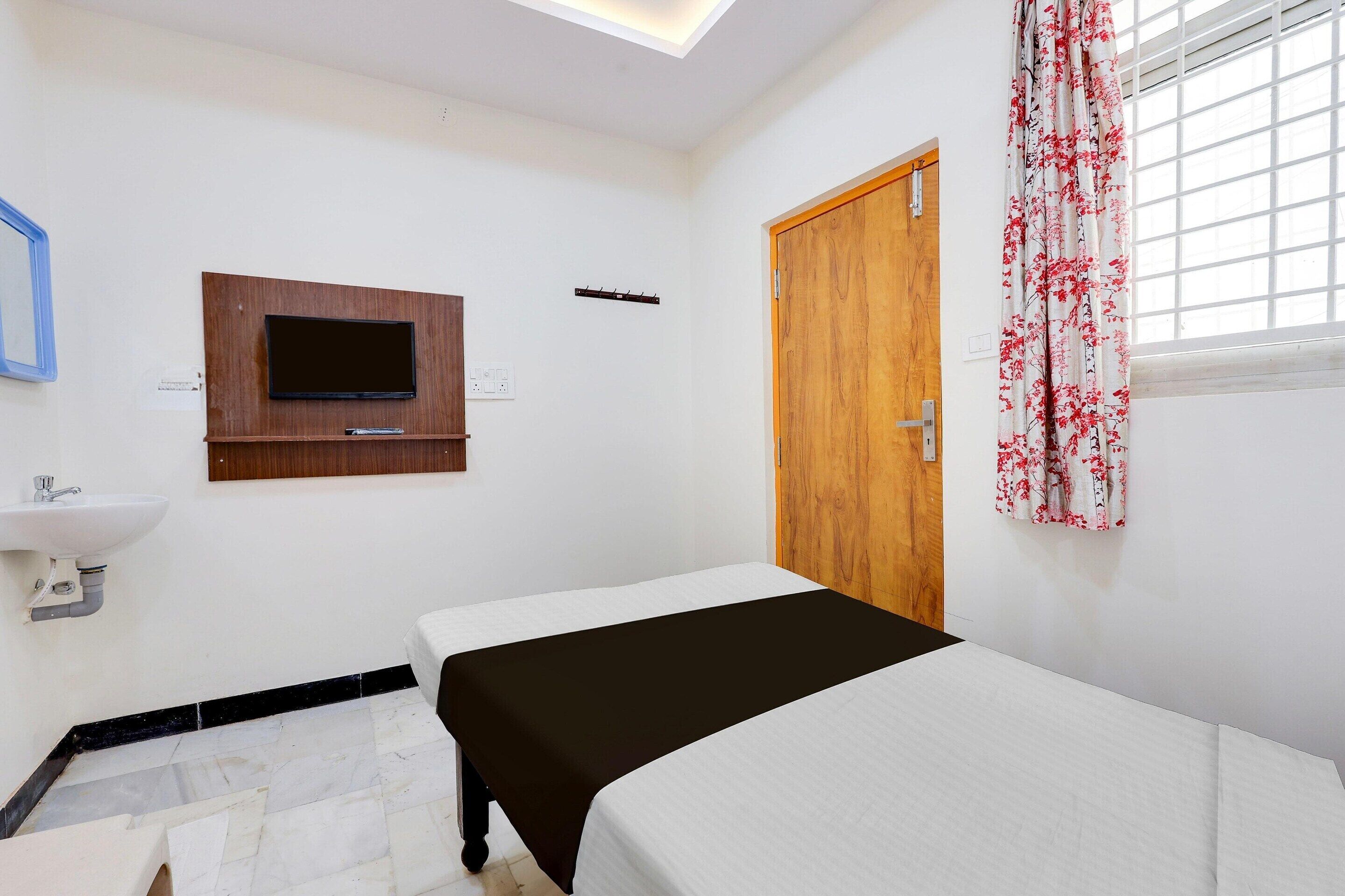 A bedroom with a bed, a TV mounted on the wall, a wooden door, and a window with curtains.
