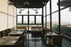 En restaurang med bord och avskilda sittplatser, stora fönster och utsikt över staden.