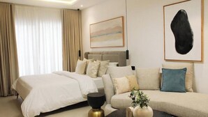 A hotel room with a bed, a sofa, a coffee table, and artwork on the walls. - Modern East Legon Studio with Private Balcony - Accra (Accra)