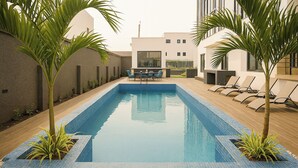 A rectangular pool with blue tiles, surrounded by lounge chairs and small palm trees. - Modern East Legon Studio with Private Balcony - Accra (Accra)