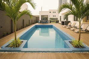 A rectangular pool with blue tiles, surrounded by lounge chairs and small palm trees. - Modern East Legon Studio with Private Balcony - Accra (Accra)