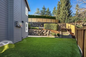 Un patio trasero residencial con un muro de piedra, una valla de madera y un césped bien cuidado.