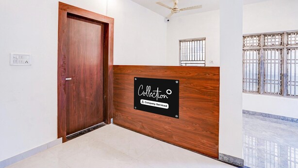 A reception area with a wooden reception desk, a ceiling fan, and a window with metal bars. - Deluxe Hotel Raj Shree (Lucknow)