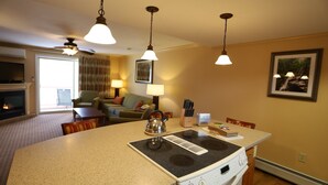 Una cocina con estufa, una mesa de comedor, sillas, un hervidor y luces en el techo.