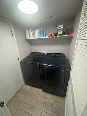 A laundry room with two front-loading washers and dryers, a shelf with cleaning supplies, and a white door. - Charming 3-bedroom house with AC in El Paso (El Paso)