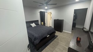 Een slaapkamer met een bed, bureau, kledingkast, plafondventilator en nachtkastje.