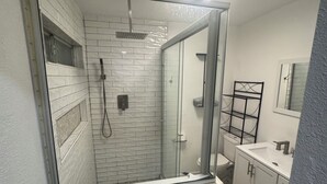 Een badkamer met een glazen douchecabine, een witte wastafel en een spiegel.