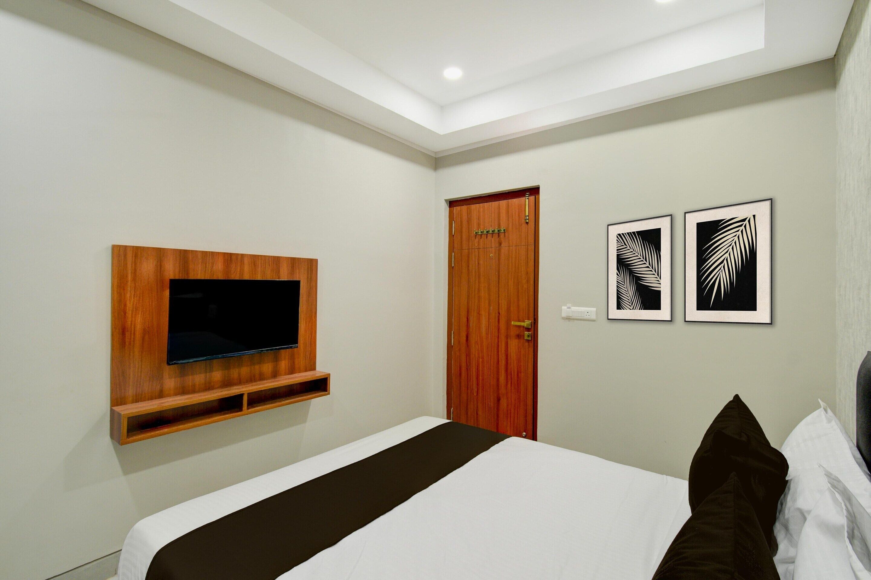 Une chambre d’hôtel avec un lit, un téléviseur fixé au mur, une porte en bois et deux motifs de feuilles encadrées sur le mur.