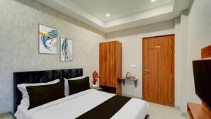 Quarto de hotel com uma cama, um guarda-roupa de madeira, uma televisão e duas pinturas abstratas na parede.