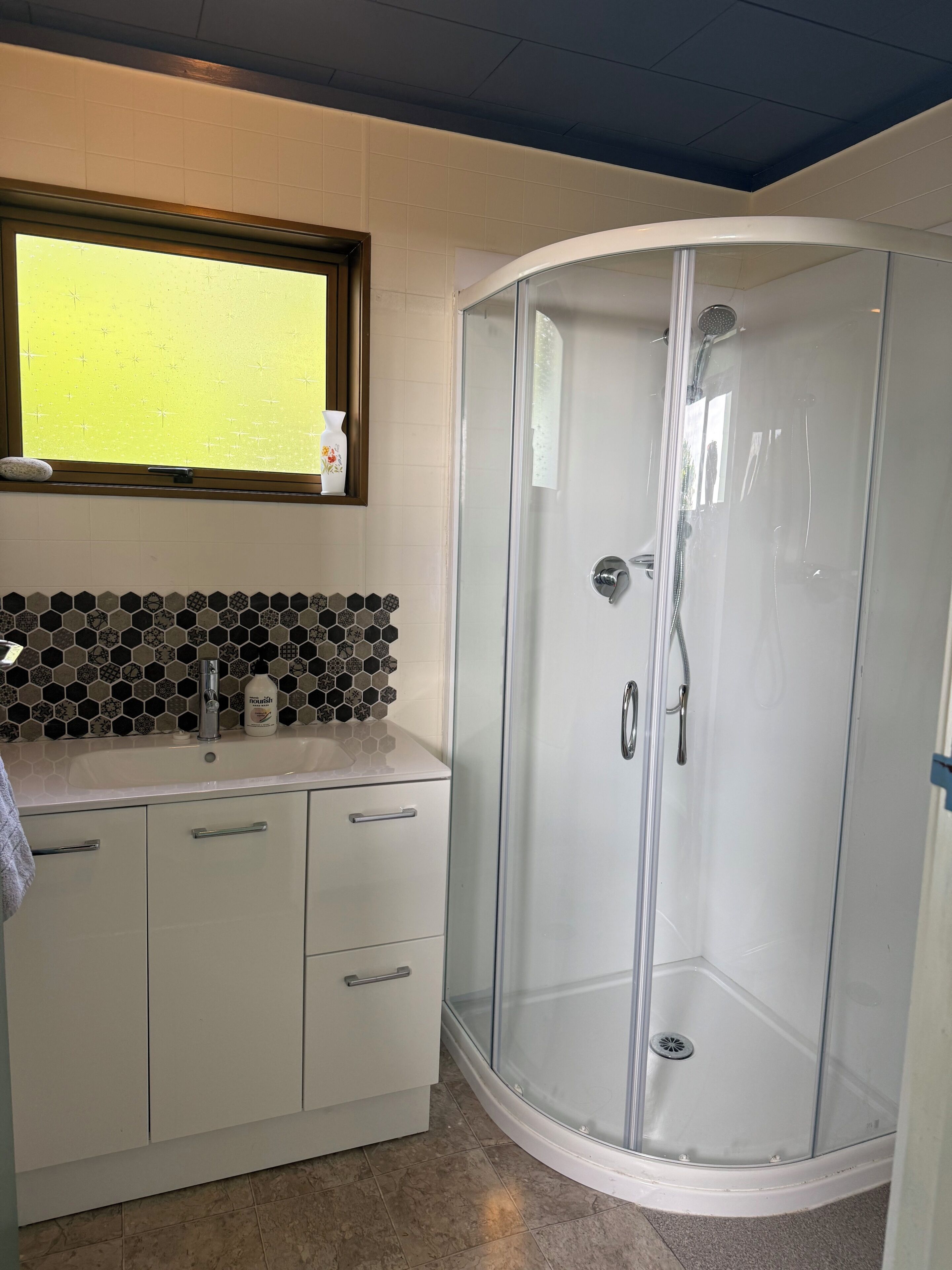 A bathroom with a glass-enclosed shower, a sink with a soap dispenser, and a tiled backsplash.