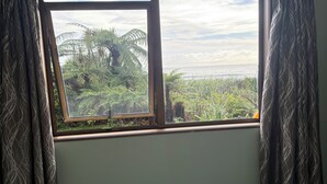 Ein Zimmer mit Bett, Fenster mit Vorhängen und Blick auf Grünflächen und Wasser.