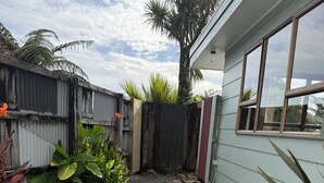 Ein Schotterweg führt zu einem Haus mit Holzzaun, einer Palme und verschiedenen Pflanzen.