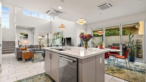 A modern kitchen with a central island, built-in appliances, and a dining area with a red chair. - "Good Times" at The Vibe - Private Spa, Views (Palm Springs)