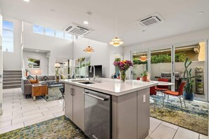 Uma cozinha moderna com uma ilha central, eletrodomésticos embutidos e um espaço de refeições com uma cadeira vermelha.