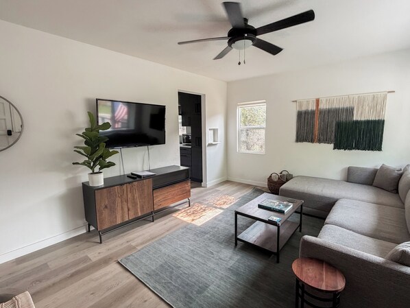 Un salon moderne doté d’un téléviseur à écran plat, d’un ventilateur de plafond, d’un canapé, d’une table basse et d’une plante.
