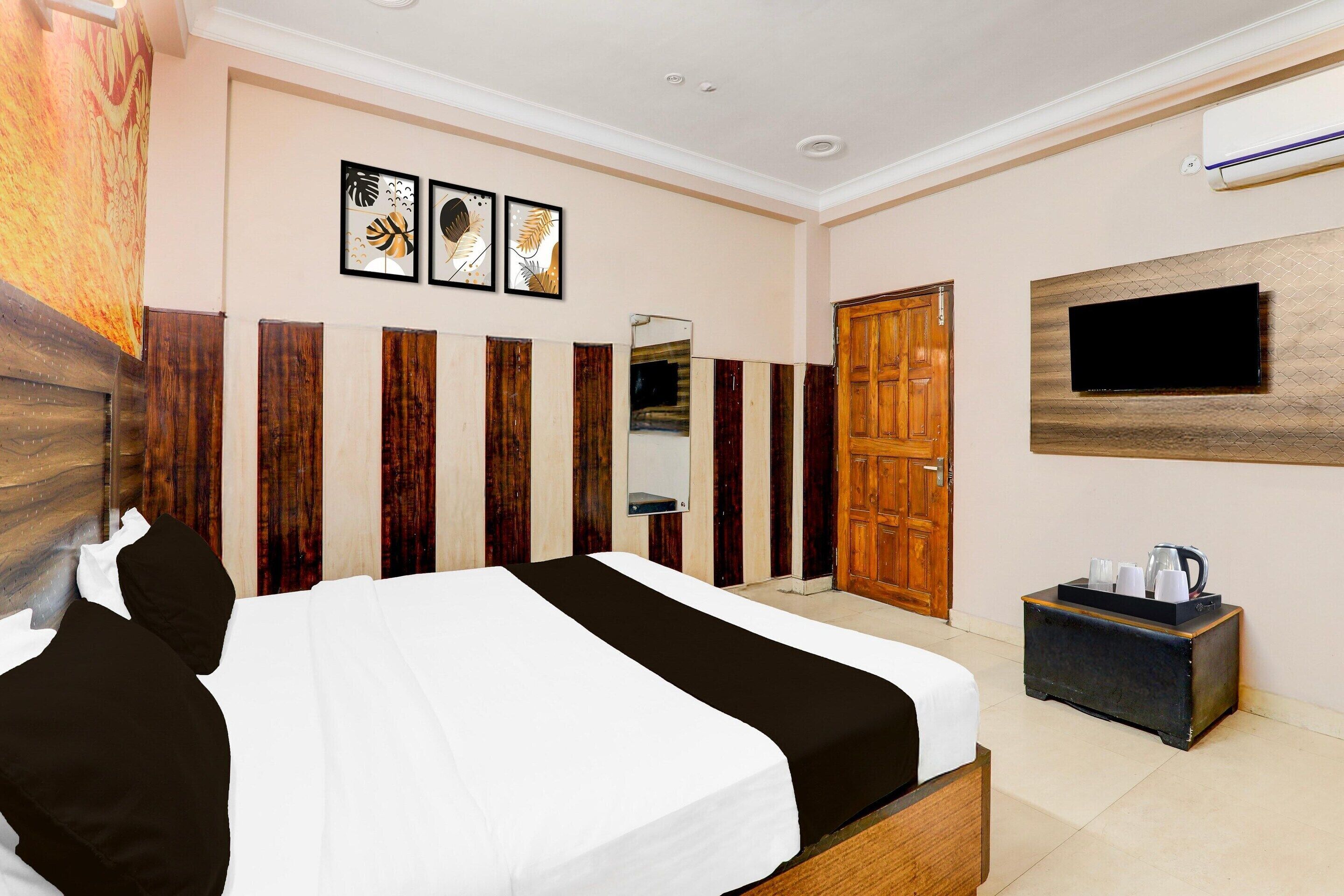 A hotel room with a bed, a television, a mirror, and a small table with a kettle.