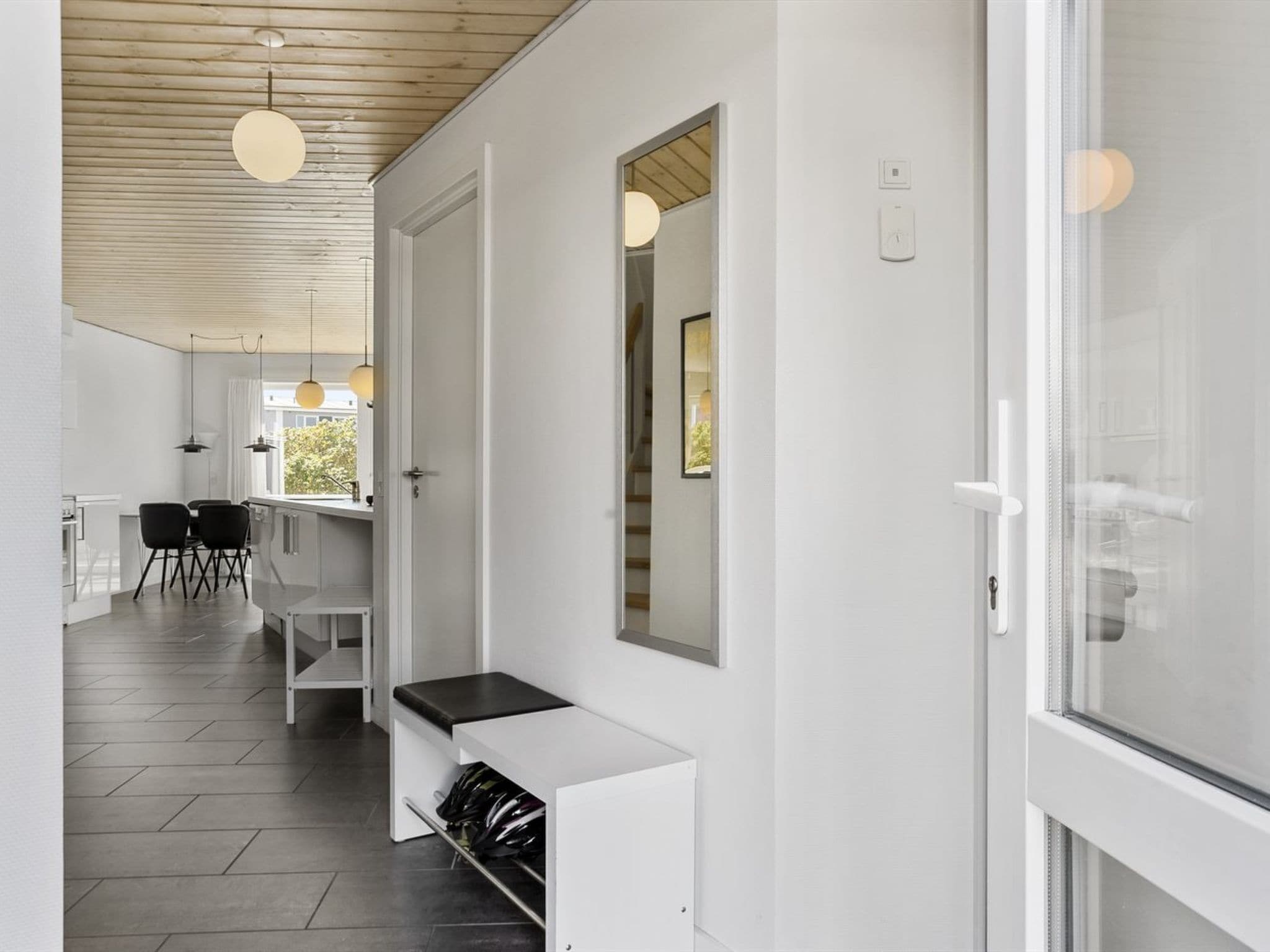 Un intérieur moderne comprenant une cuisine, un coin repas et un couloir menant à une porte vitrée.