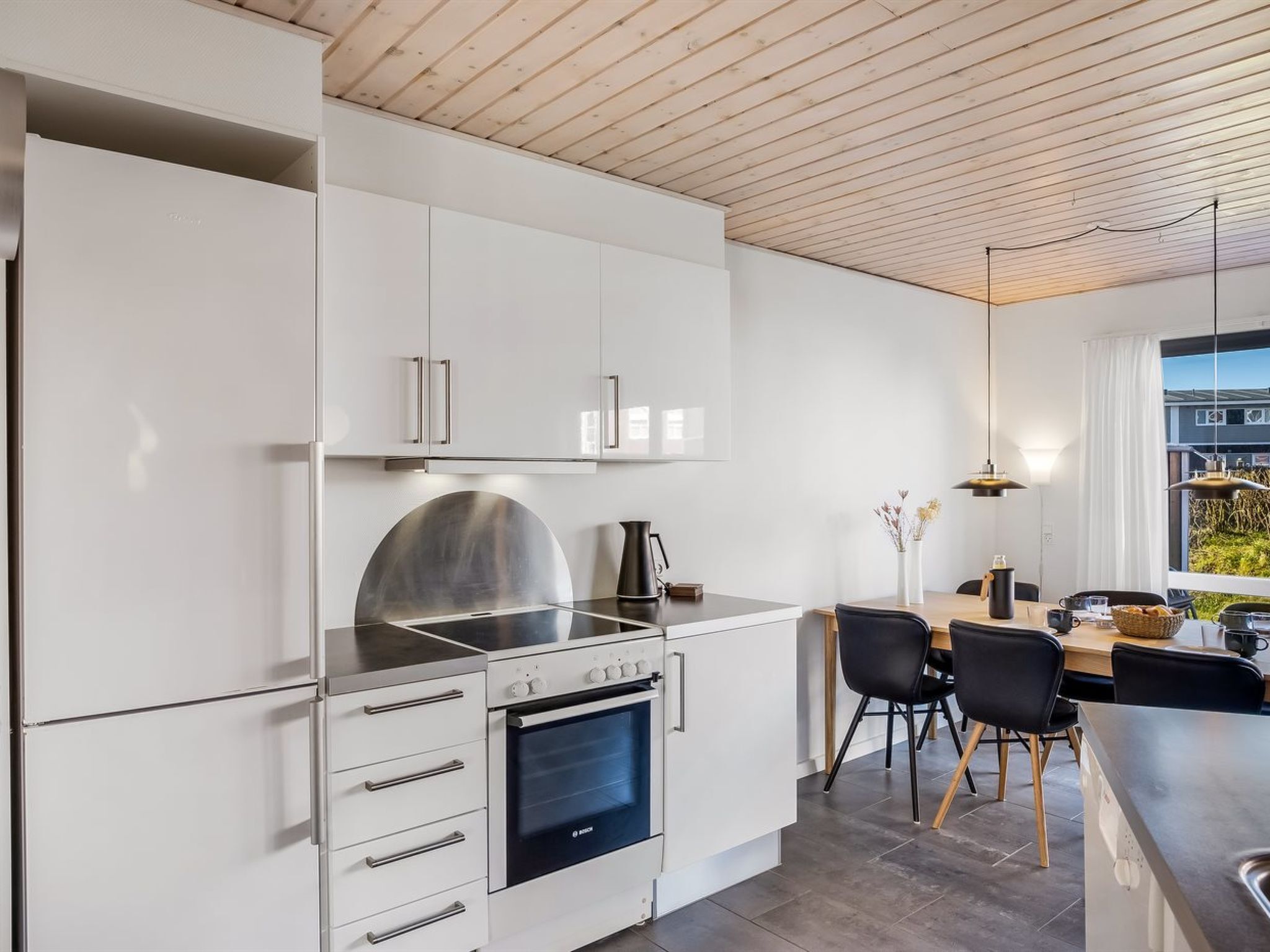 Eine moderne Küche mit weißen Schränken, einem Backofen von Bosch und einem Essbereich mit Blick.
